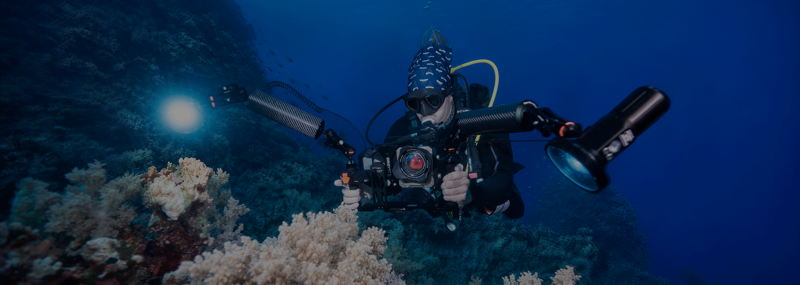 Underwater diver exploring coral reef with DIVEVOLK SeaTouch6 pro housing rig — dual handle tray setup with video lights for professional underwater photography and videography