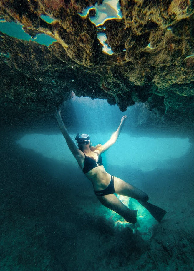 A snorkeler captured in a graceful pose underwater near a rocky cave, shot with the SeaTouch 4 Max Plus Housing, highlighting the beauty and tranquility of underwater human subjects.