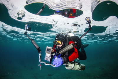 A striking underwater shot of Slava Simakov in full ice diving gear, surrounded by bubbles as he ascends.