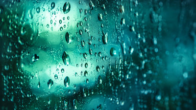 Backlit water droplets on glass in teal light