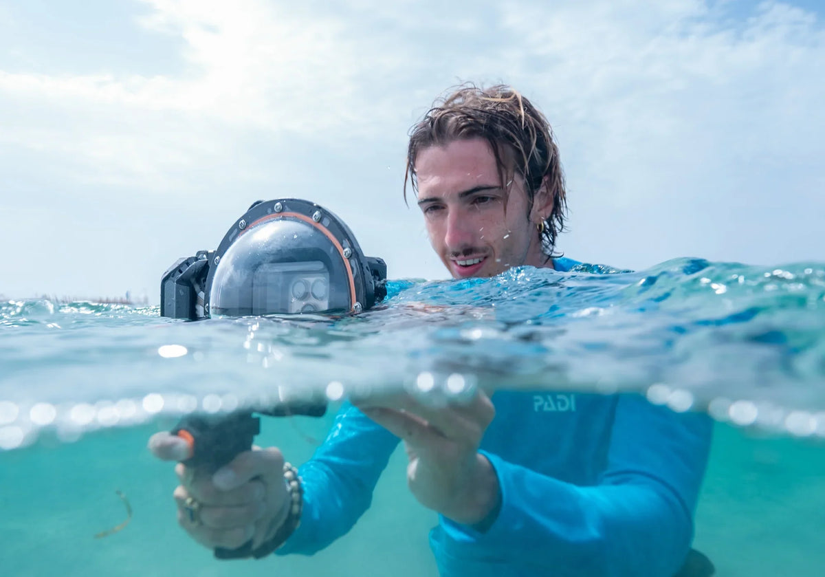 Snorkeler at the water surface holding a DIVEVOLK SeaTouch 6 Pro housing with a dome lens for a split shot