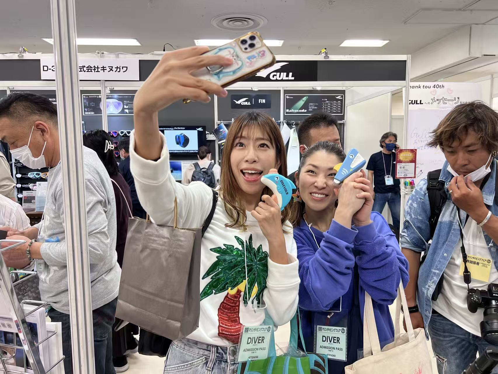 Happy visitors taking a selfie with a DIVEVOLK housing at a dive show, illustrating the joy of the community.