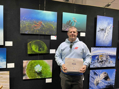 Sean Elliott standing proudly next to his award-winning photo on display at the Go Dive Expo.
